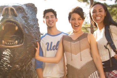 Three students smile for a photo with The Bruin statue.